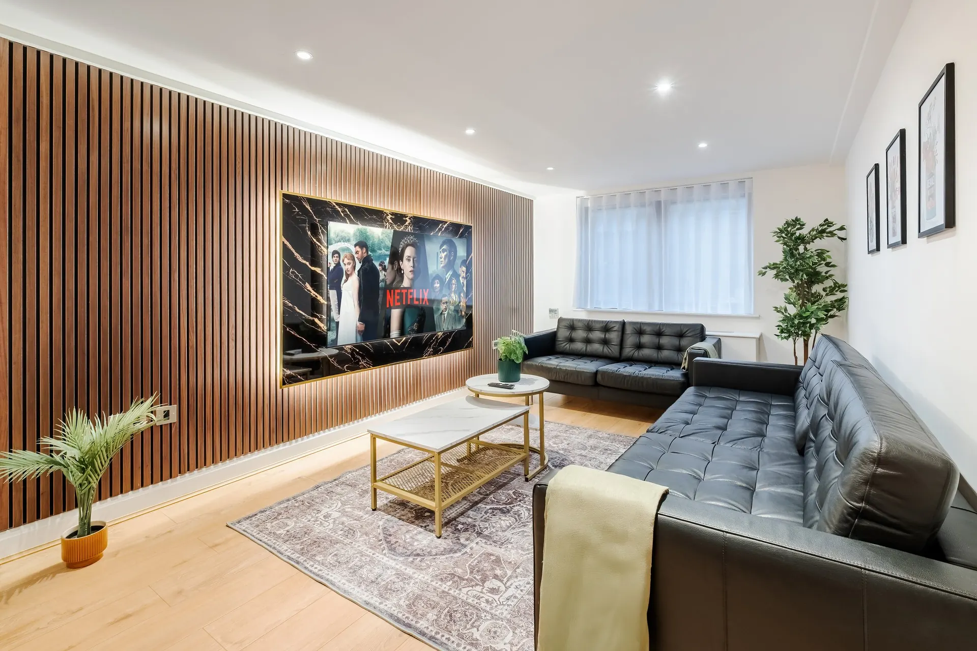Living room with black leather sofas and a 75 inch TV on an oak panel wall