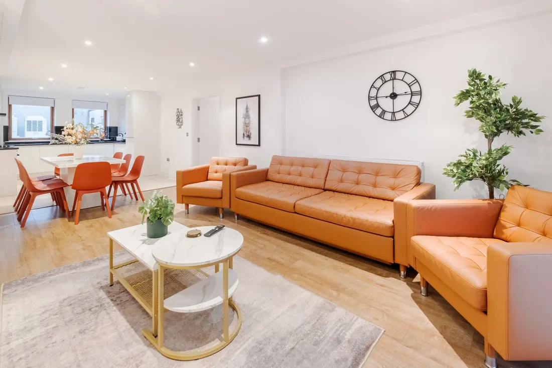 Three orange leather sofas around a marble coffee table, with the dining table by the windows