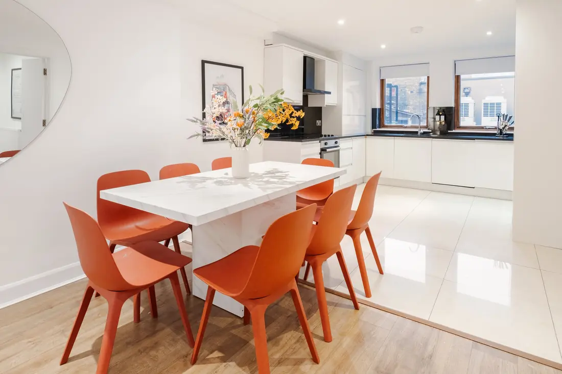 Dining table for eight with orange chairs and the kitchen behind