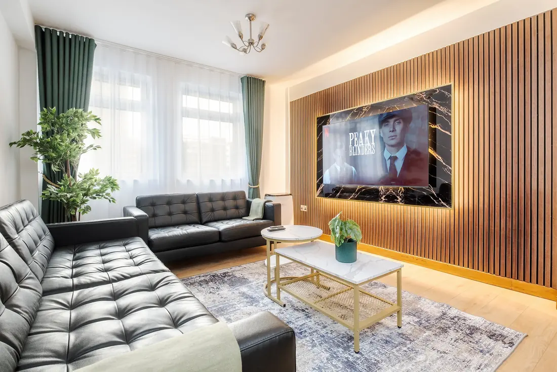Living room with black leather sofas and a 75 inch TV on an oak panel wall