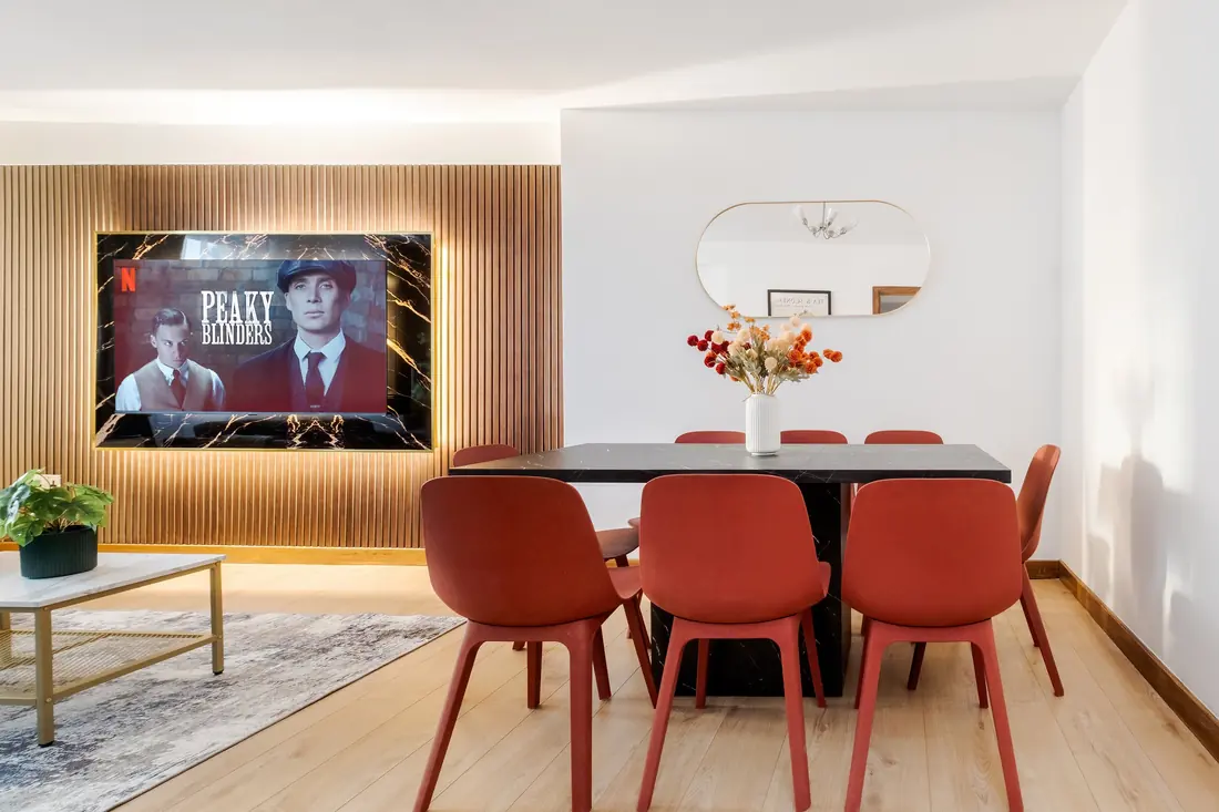 Dining table for six with red chairs beside the TV wall