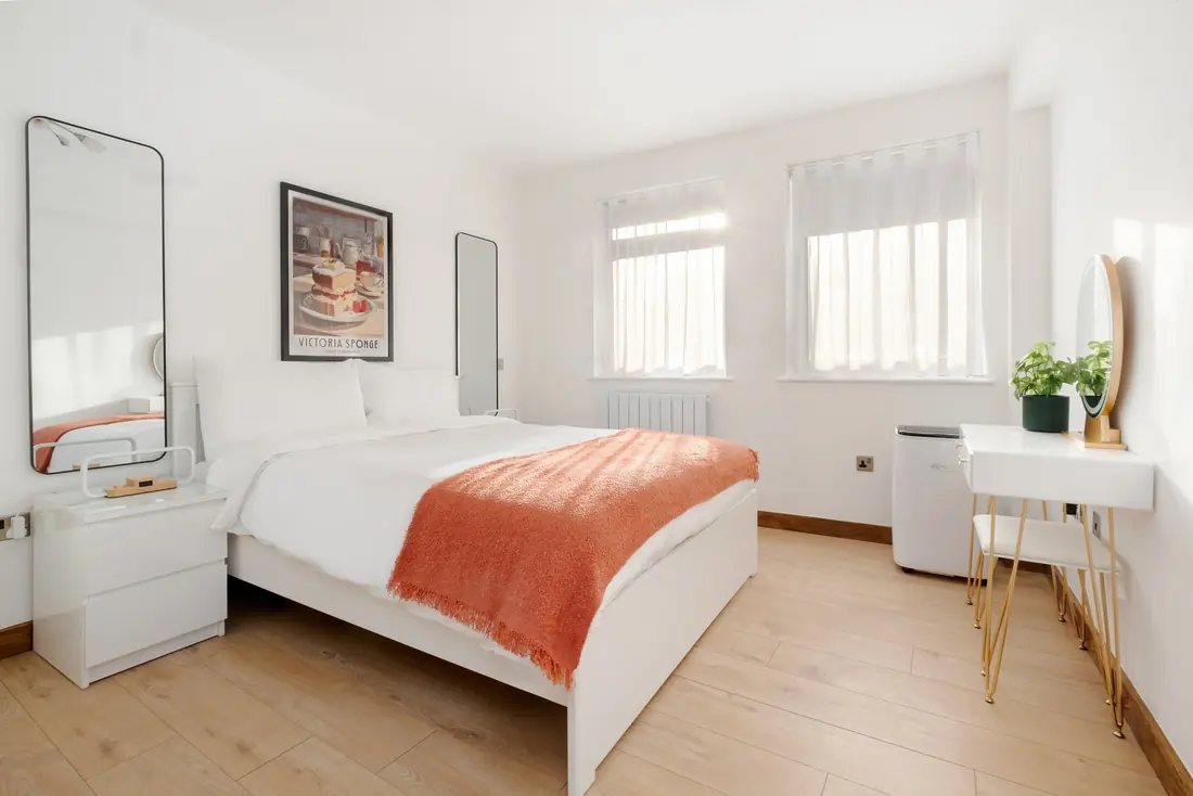 King bedroom with an orange throw and a Victoria sponge print